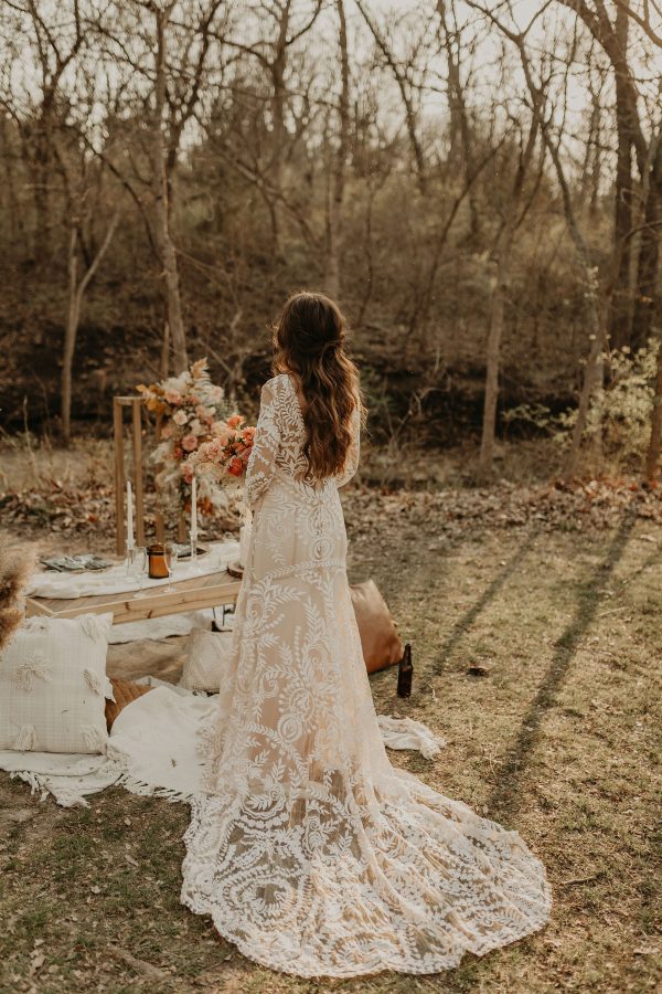A picnic set up in the woods with a bride posing with a bohemian lace wedding dress