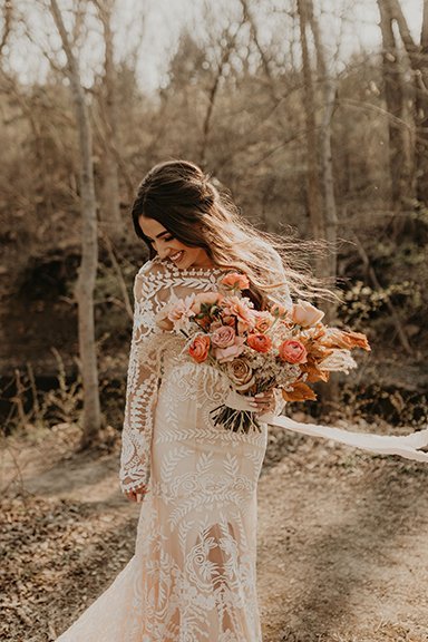 A gorgeous bride holding a bouquet to her chest, wearing a bold lace boho wedding dress