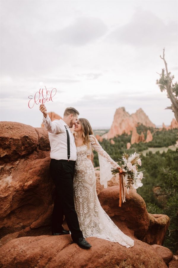 Bride and Groom embracing in the Garden of the Gods, dressed eloping in a suit and boho wedding gown