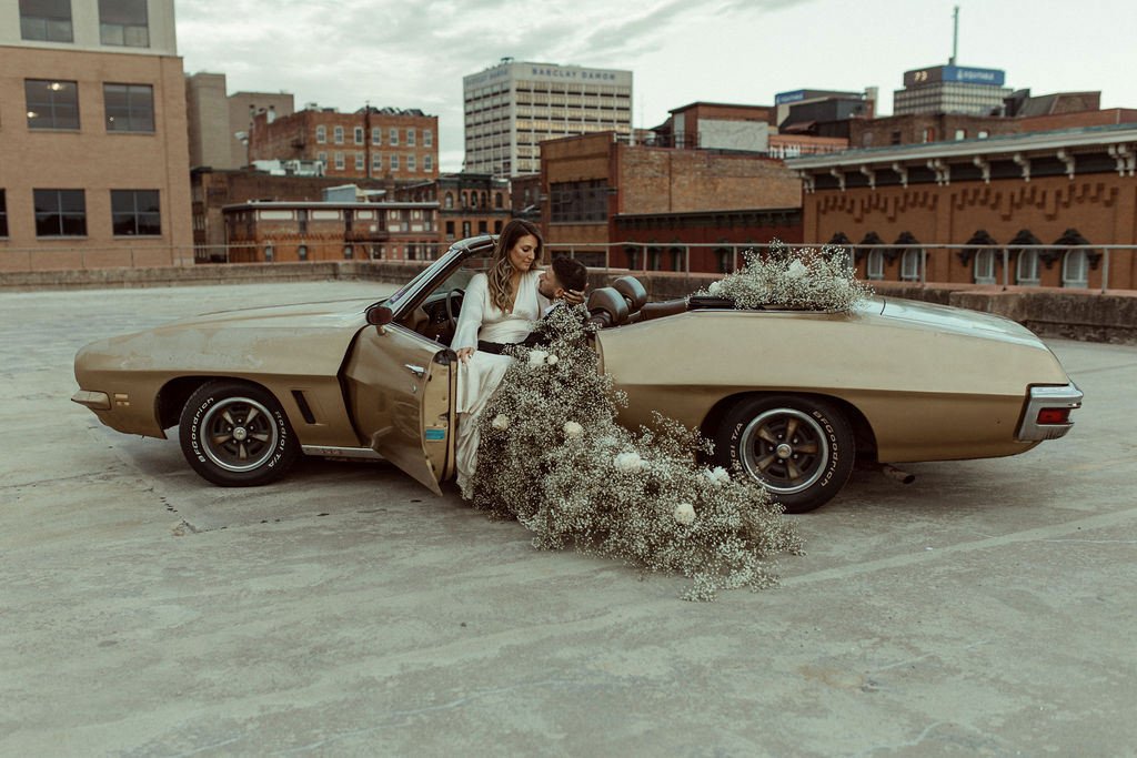 Vintage car on the top of a city rooftop, decorated with baby's breath and a couple in wedding attire
