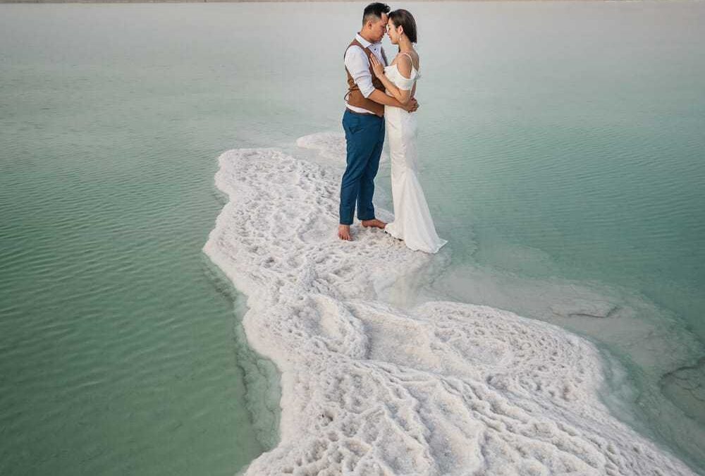 image of a bride and groom who had a destiation wedding or elopement at the dead sea. They are standing at the end of a large salt bar in the dead sea.